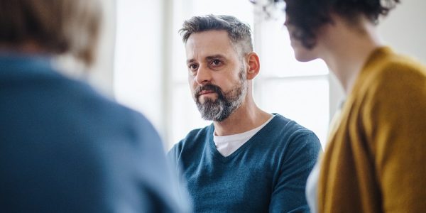 Midsection of men and women sitting in a circle during group therapy, talking.