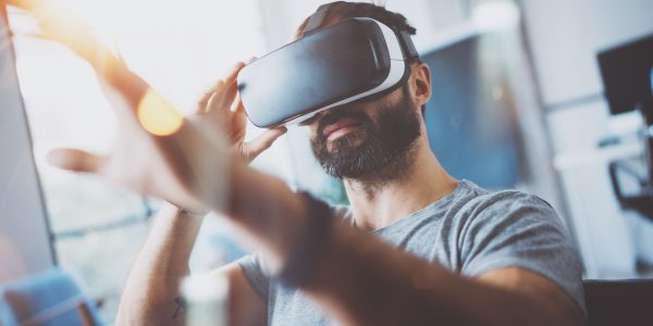 Closeup of bearded young man wearing virtual reality goggles in modern coworking studio. Smartphone using with VR headset. Horizontal, blurred.